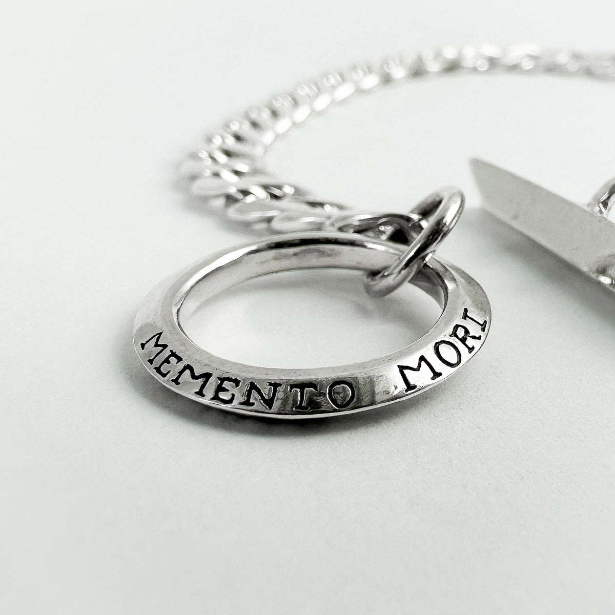 A silver chain bracelet with a circular ring charm engraved with 'MEMENTO MORI' 