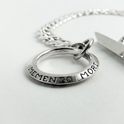 A silver chain bracelet with a circular ring charm engraved with 'MEMENTO MORI' 
